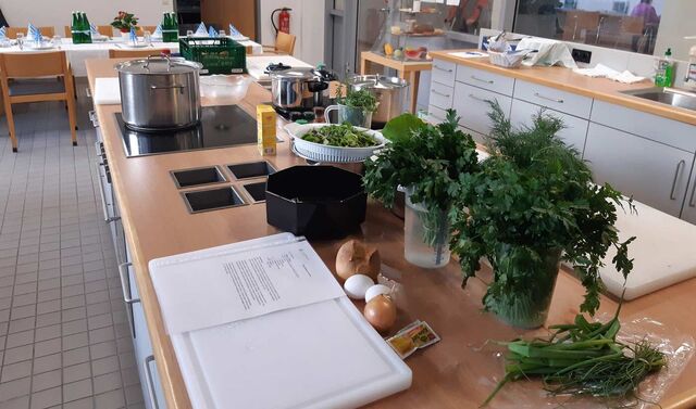 Die Küche ist bereit für die Teilnehmer am Kochevent. Schneidebretter, Gemüse und Kräuter stehen bereit.