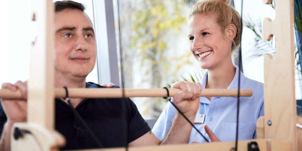 Junge Therapeutin überwacht Patienten bei der Ausführung einer Übung am Gerät.