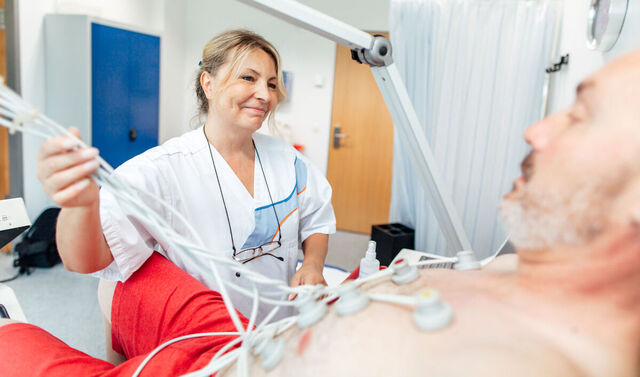 Krankenpflegerin führt bei einem Patienten ein EKG durch.