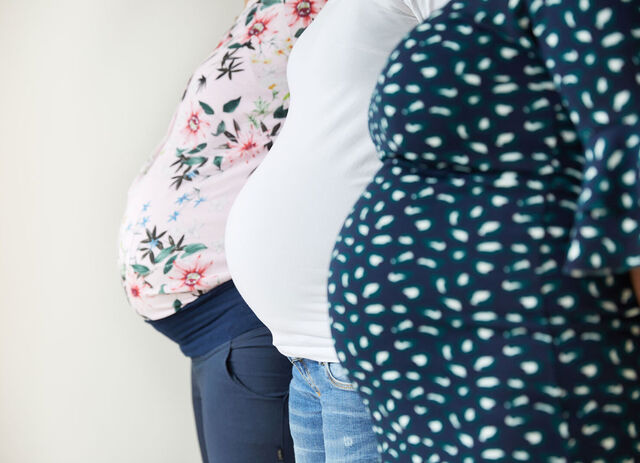 Drei schwangere Frauen zeigen hintereinander stehend ihren Babybauch in die Kamera