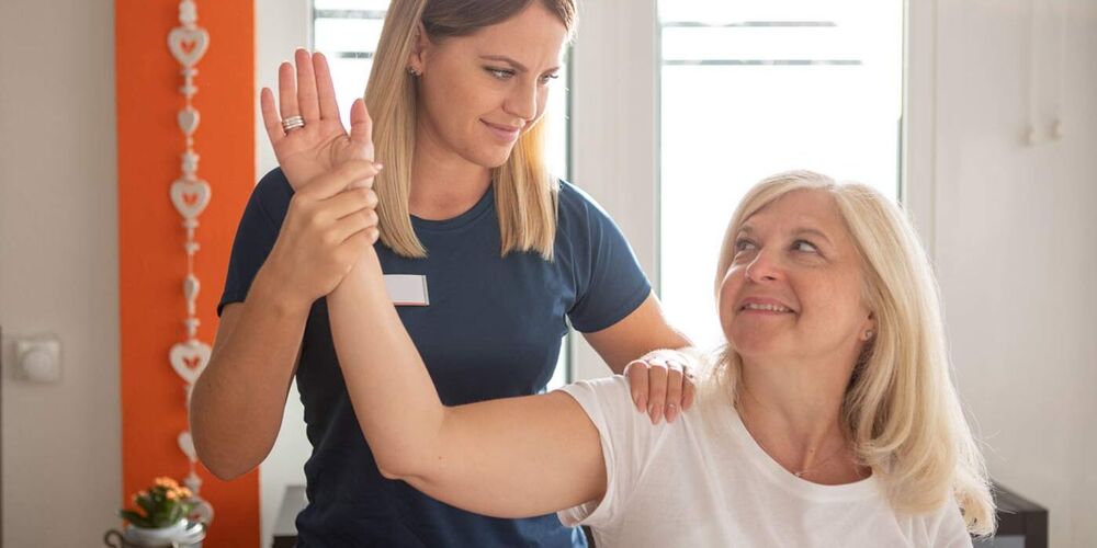 Physiotherapeutin hält den Arm einer Patientin in der Hand und bewegt diesen.