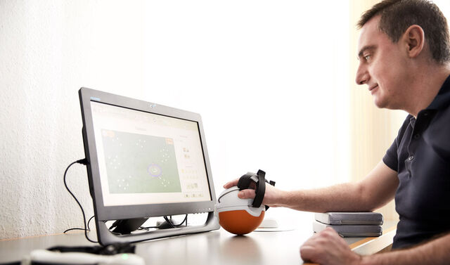 Patient sitzt am Computer und trainiert seine Hand.